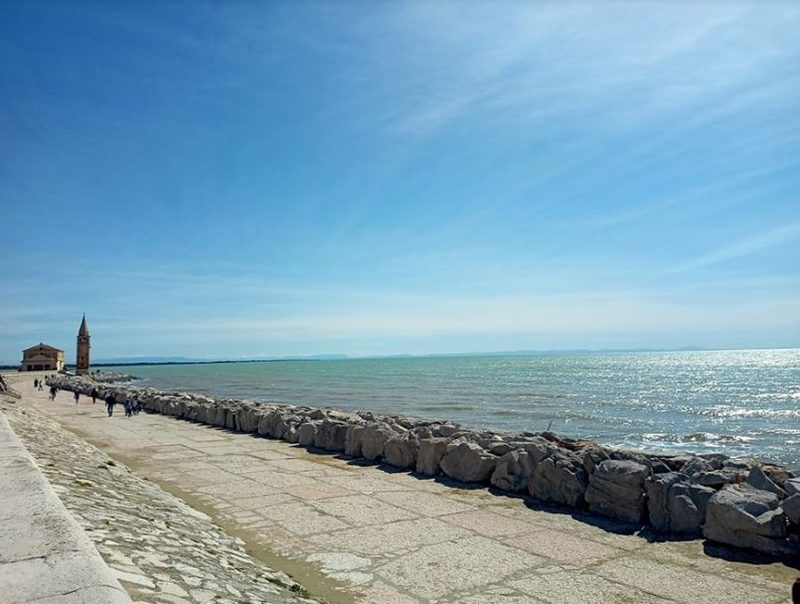 Passeggiata sul molo di Caorle con la scogliera e il campanile sullo sfondo